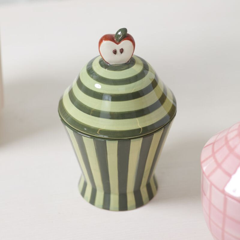Decorative ceramic jar with striped design and apple-shaped lid on a light surface.