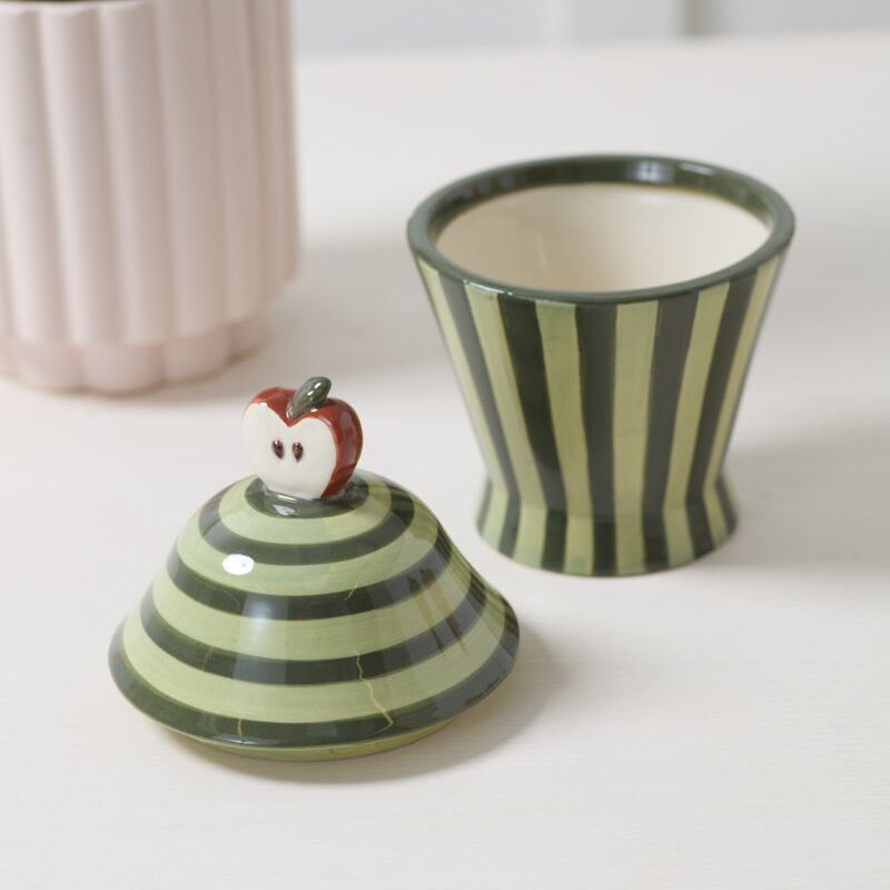 Green striped ceramic canister with a lid featuring a small apple handle on a white surface.