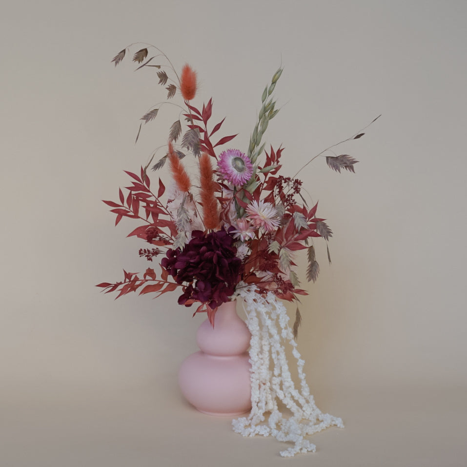 Pink vase with dried flowers against a beige background
