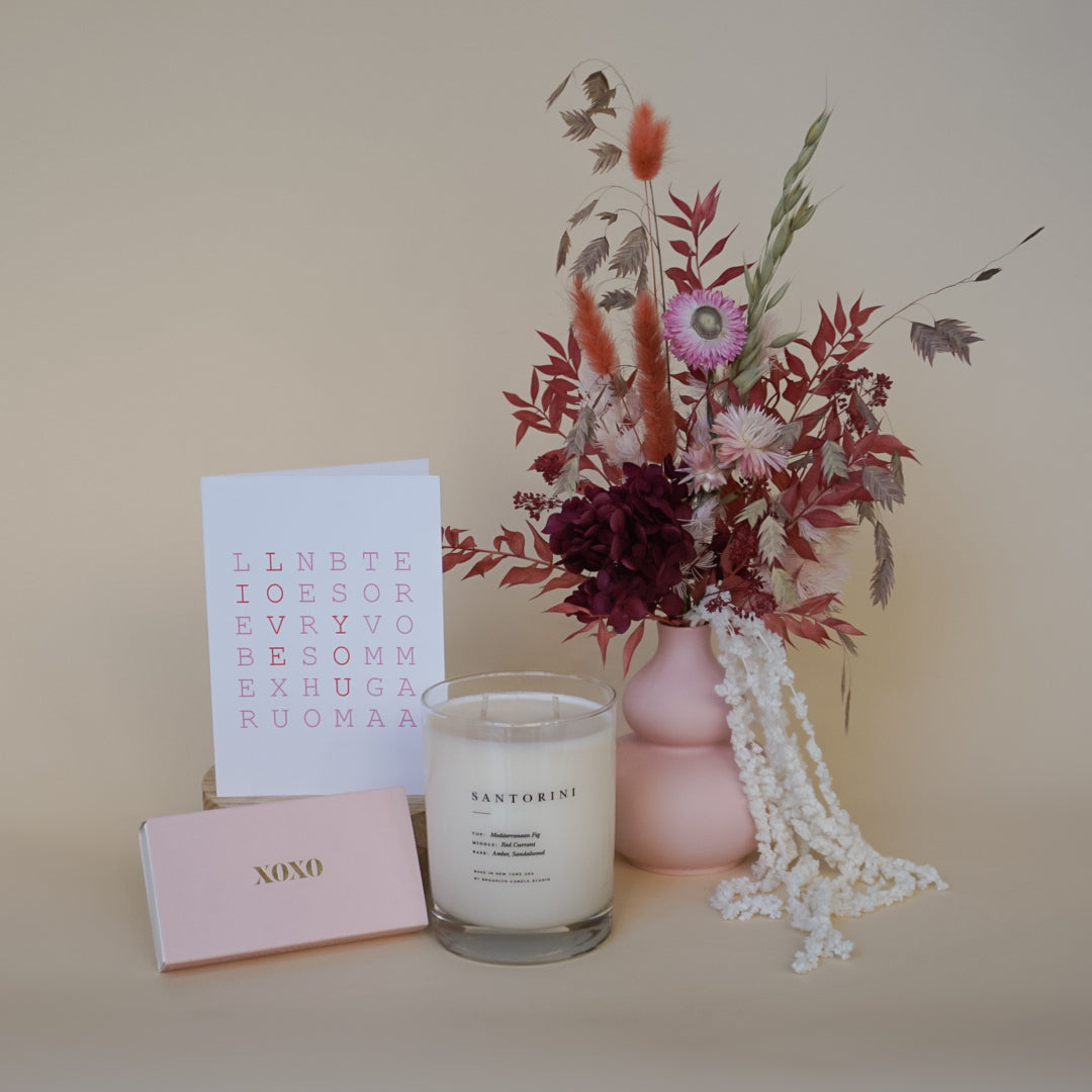 Candle, card, and vase with dried flowers on a beige surface