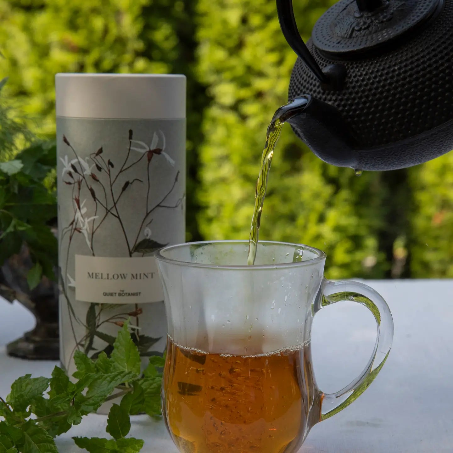 Tea being poured into a glass mug with a tea packaging and teapot in the background.
