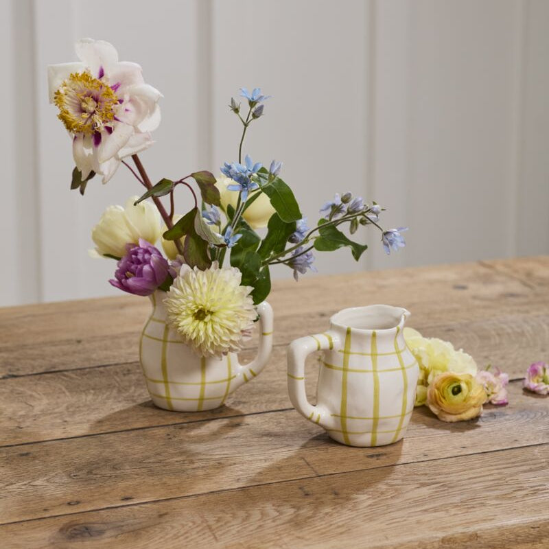 Two small pitcher vases with floral arrangements on a wooden table.