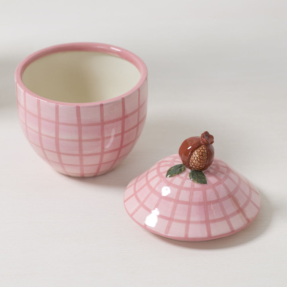 Pink checkered ceramic canister with a fruit styled lid on a white surface