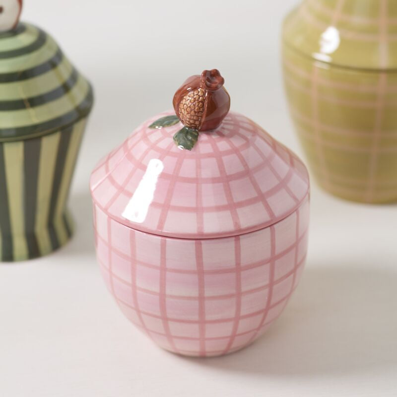 Pink ceramic jar with a grid pattern and a small decorative element on a white surface.