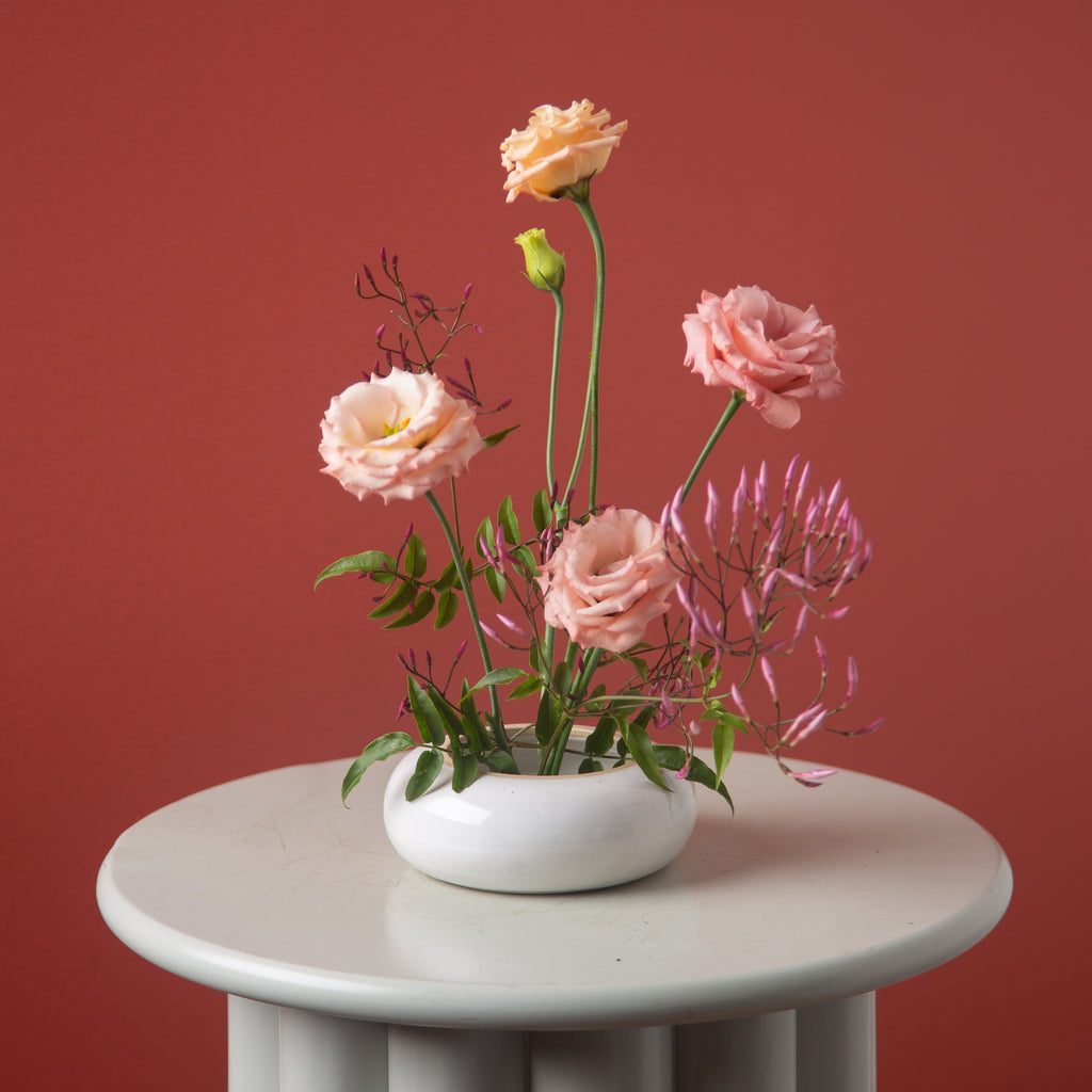 White vase with pink flowers on a gray pedestal against a red background