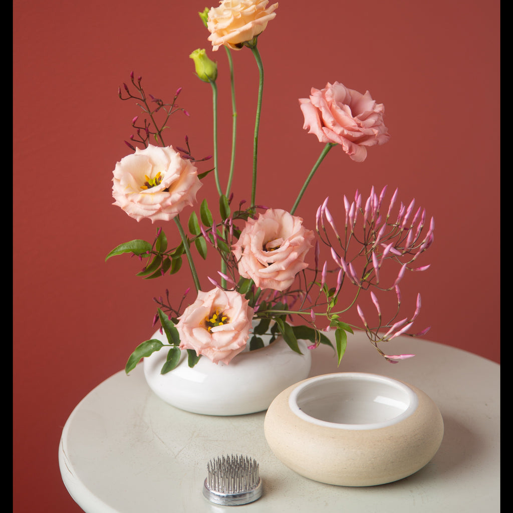 Ikebana arrangement in a white vase on a round table with a red background