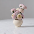 Small raw textured vase with pink and white flowers on a marble surface against a gray background