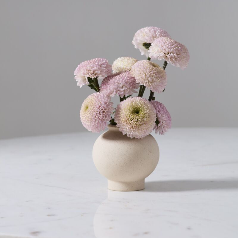 Small raw textured vase with pink and white flowers on a marble surface against a gray background