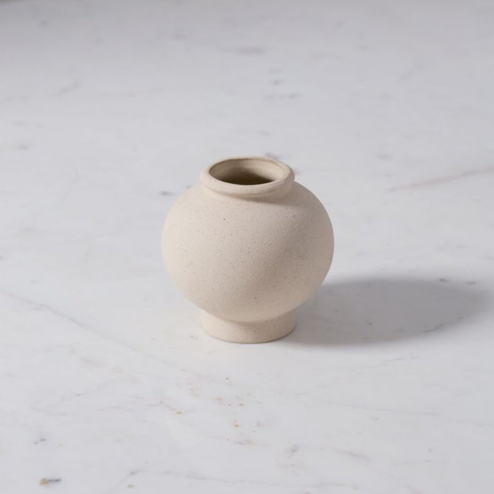 Small beige raw textured ceramic vase on a marble surface